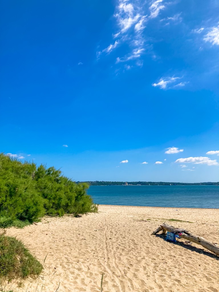A secluded stretch of Lepe Beach on a sunny day, with a view of sailing boats on the sea.